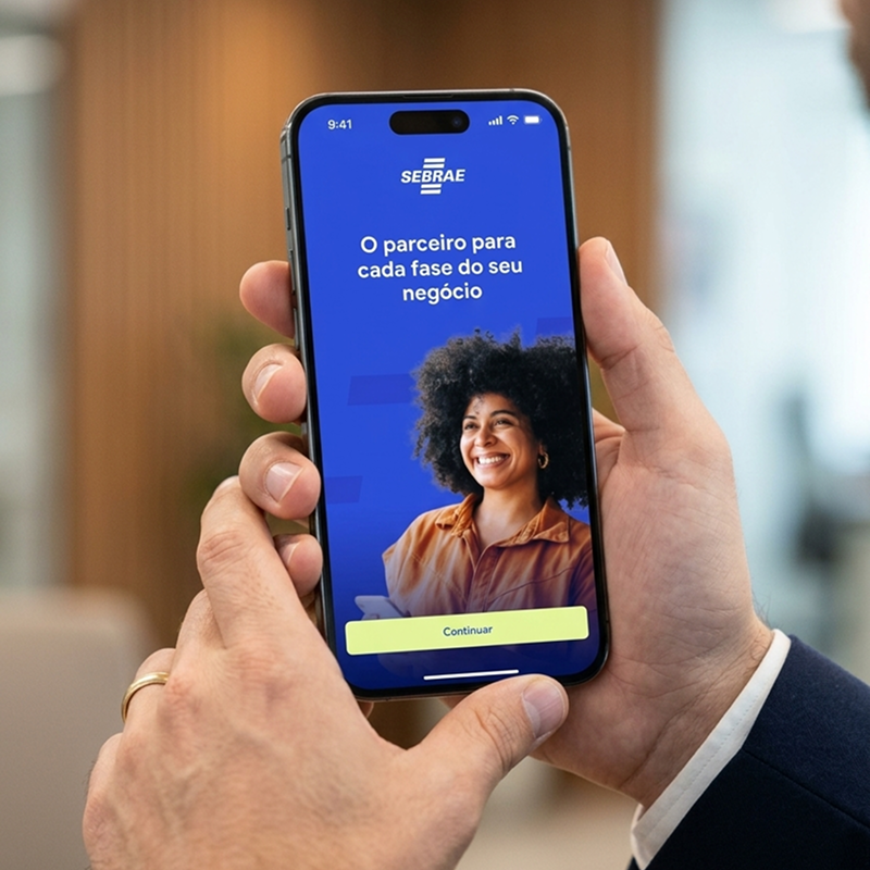 Hand holding a phone showing the Sebrae app welcome screen